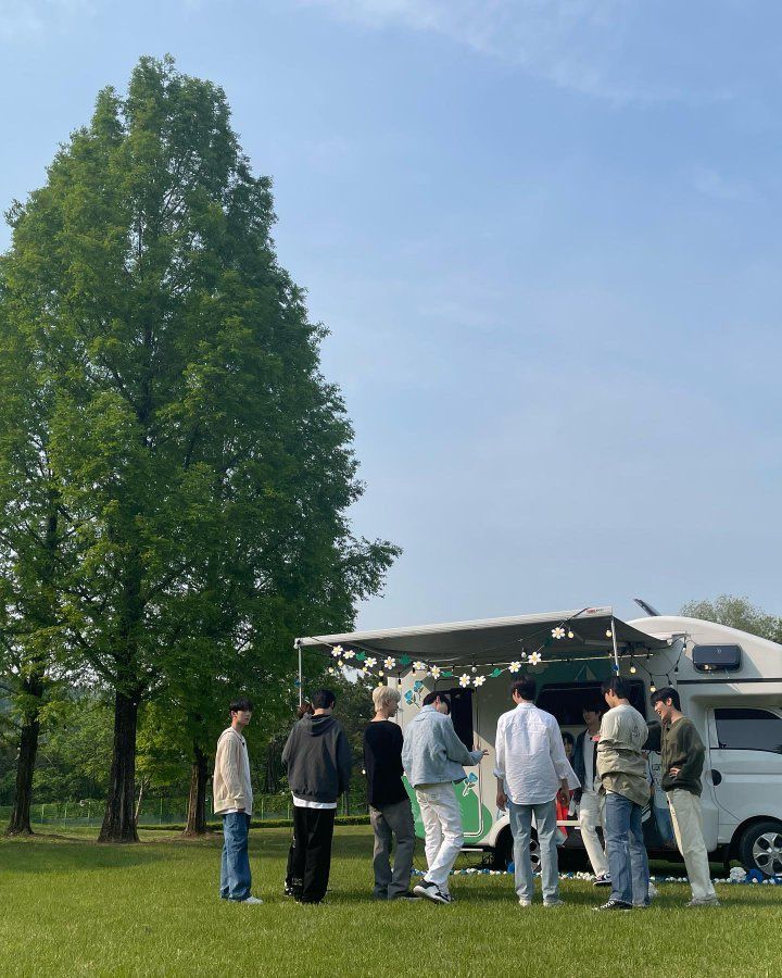 a group of people standing in front of a food truck on top of a lush green field