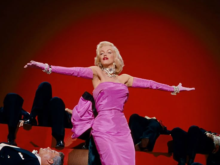 a woman in a pink dress is dancing on stage with her arms outstretched and legs spread out