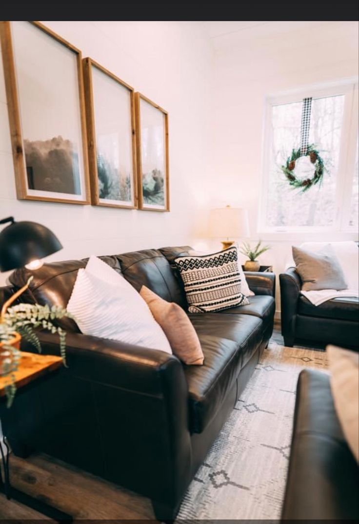 a living room with black leather couches and pictures on the wall above them, in front of a window