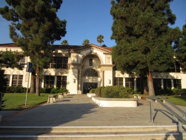 a large white building with lots of trees in the front yard and stairs leading up to it