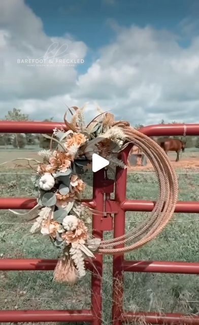 a wreath on top of a red fence in front of a horse grazing behind it