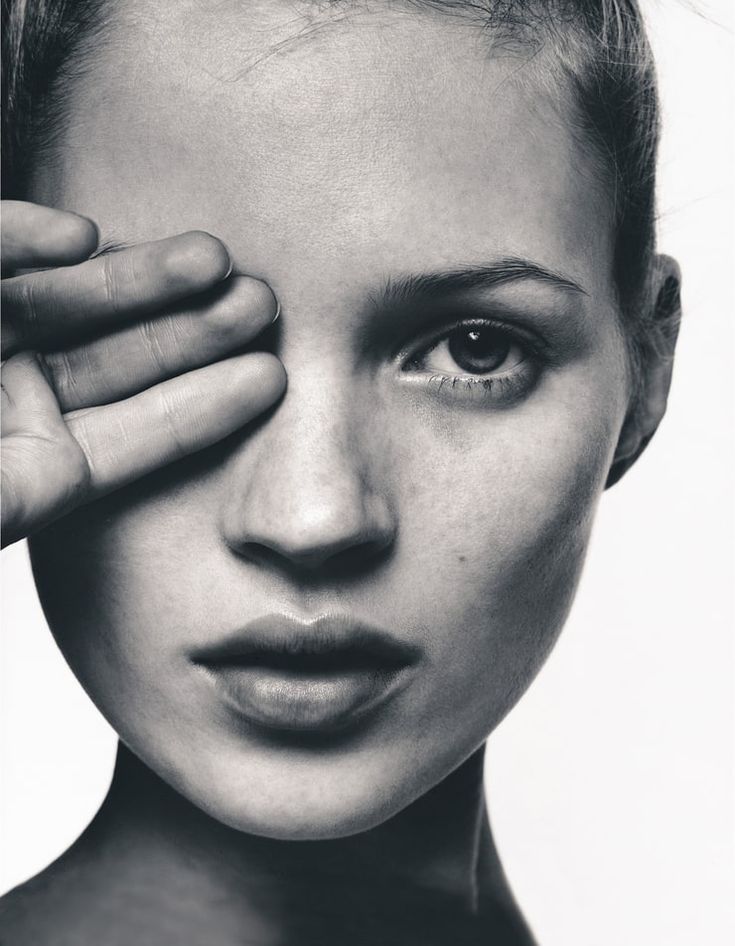 a black and white photo of a woman holding her hand to her face with one eye open