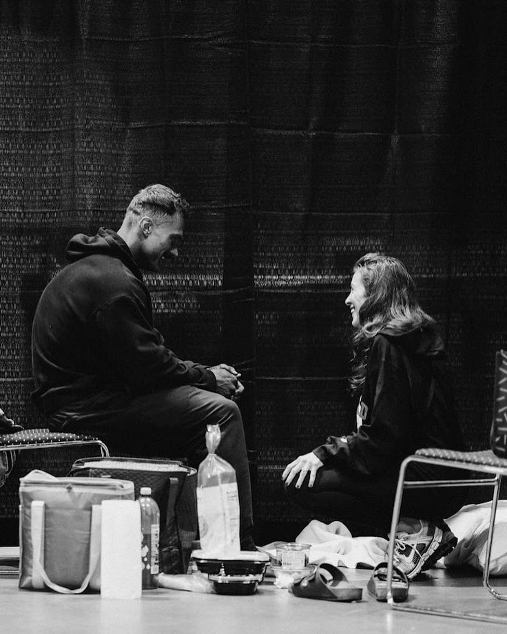 black and white photograph of two people sitting on chairs in front of a brick wall