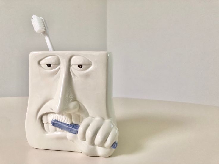 a ceramic toothbrush holder with a face on it's side holding a toothbrush