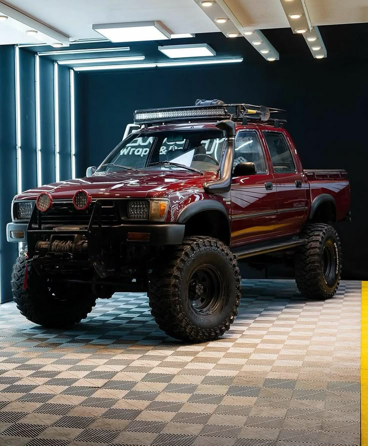 a red pick up truck parked in a garage next to a black and white checkered floor