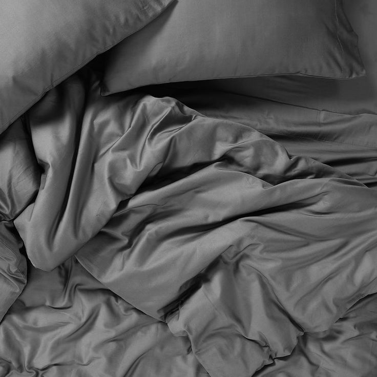 an unmade bed with grey sheets and pillowcases on top of each other