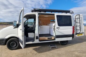 a white van parked on top of a sandy beach next to the ocean with its doors open