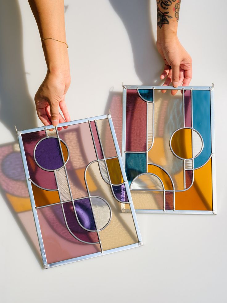 two pieces of stained glass being held by someone's hands on a white surface