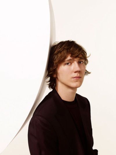 a young man standing in front of a white wall