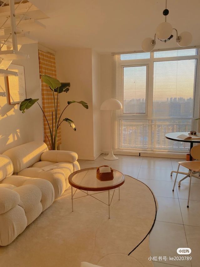 a living room filled with white furniture next to a large window covered in plants and windows