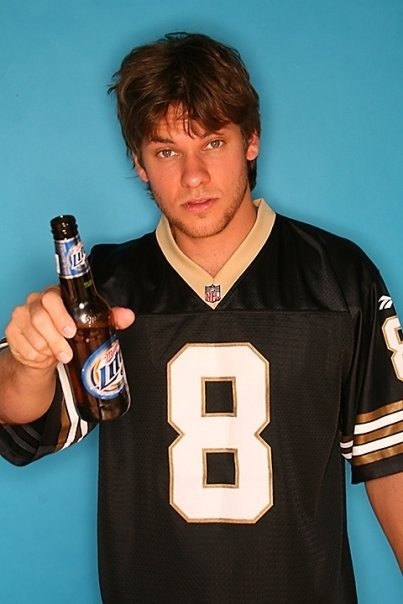 a young man holding a beer bottle and pointing to the camera while wearing a football jersey