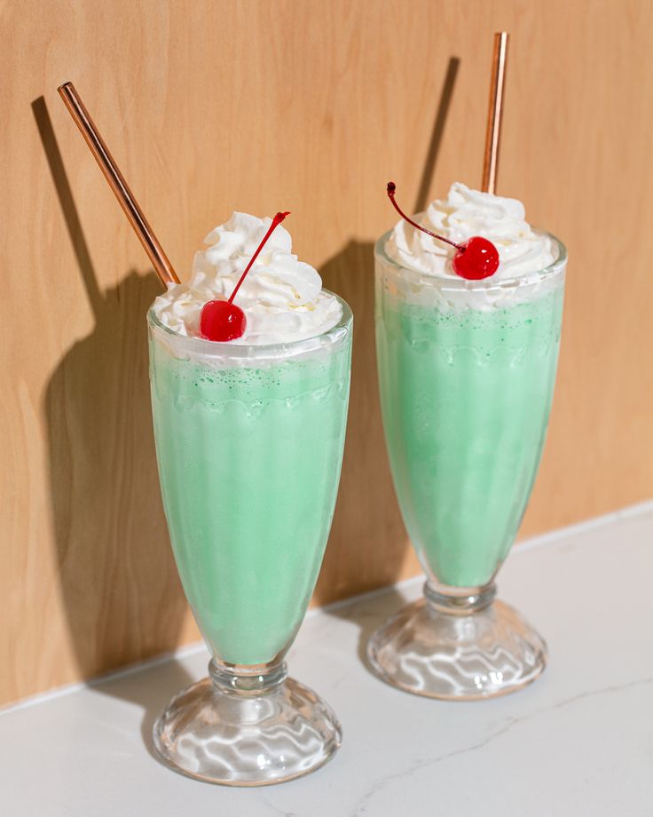 two glasses filled with green liquid and topped with whipped cream, cherries and strawberries