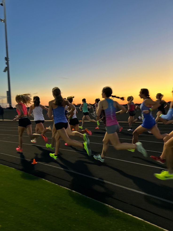 a group of people running on a race track at sunset or sunrise with the sun setting behind them