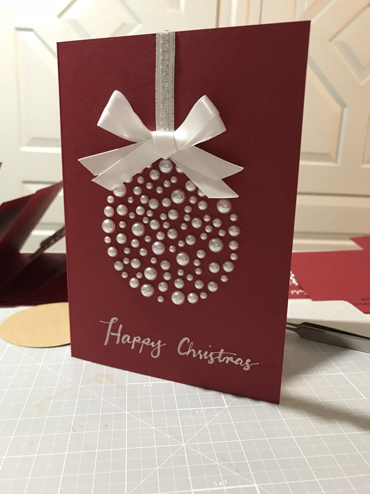 a red card with white bows and pearls on it, sitting on a table next to scissors