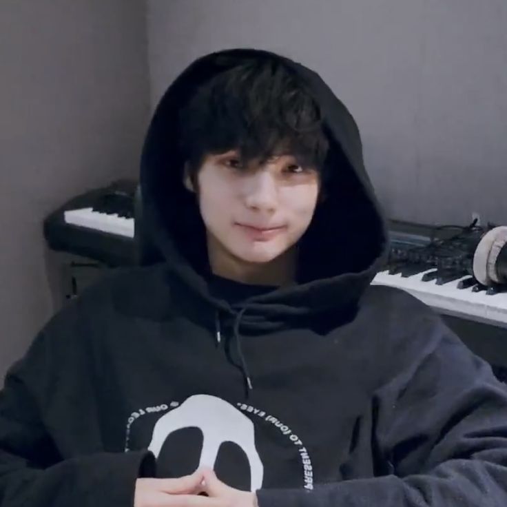 a young man wearing a black hoodie sitting in front of a keyboard