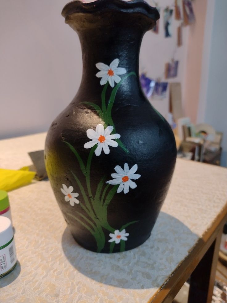 a black vase with white daisies painted on it sitting on top of a table