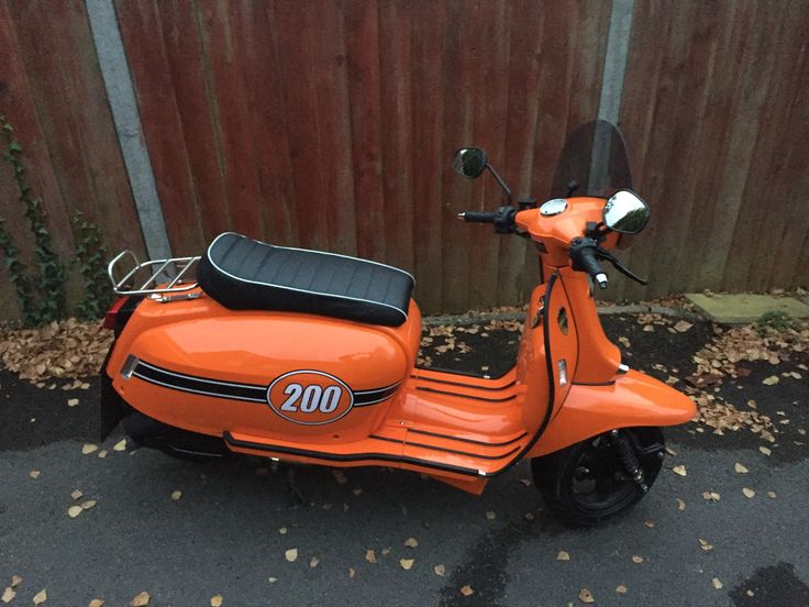 an orange scooter parked in front of a wooden fence