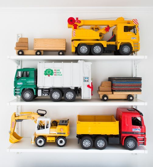 toy trucks and construction vehicles are lined up on white shelves in a playroom or bedroom