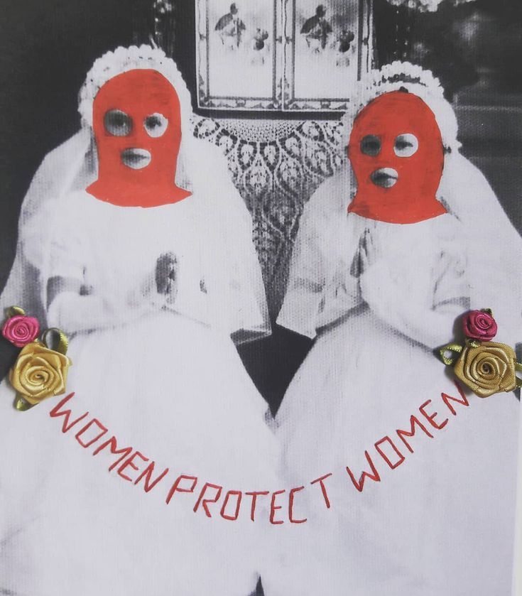 two women in white dresses and red masks with roses on their heads are facing each other