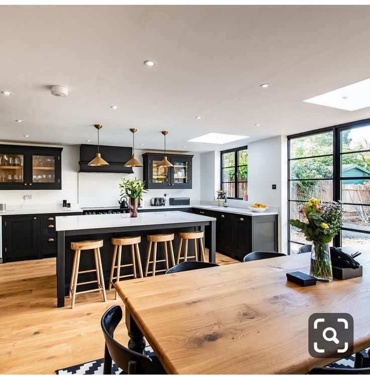 an open kitchen and dining area with wooden table, bar stools and black cabinets