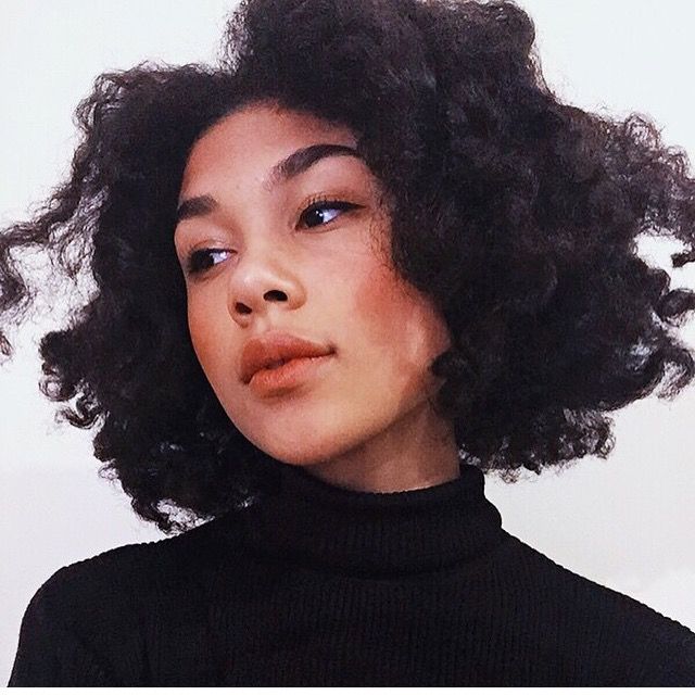 a woman with curly hair wearing a black turtle neck sweater