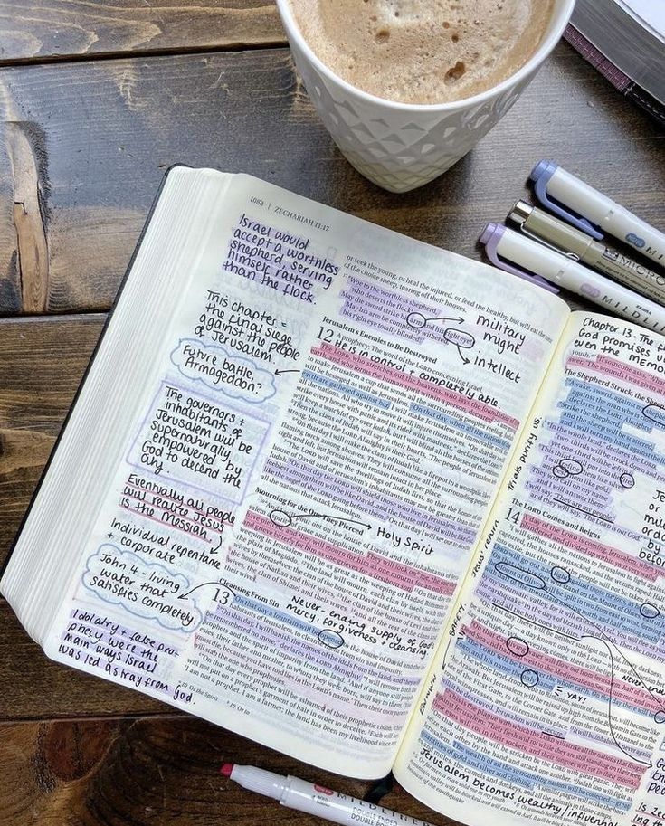 an open bible next to two pens and a cup of coffee