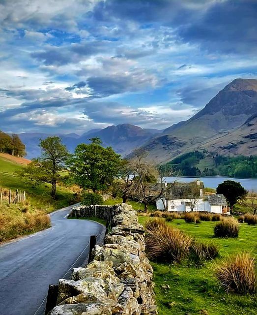 a stone wall on the side of a road next to a field and mountain range