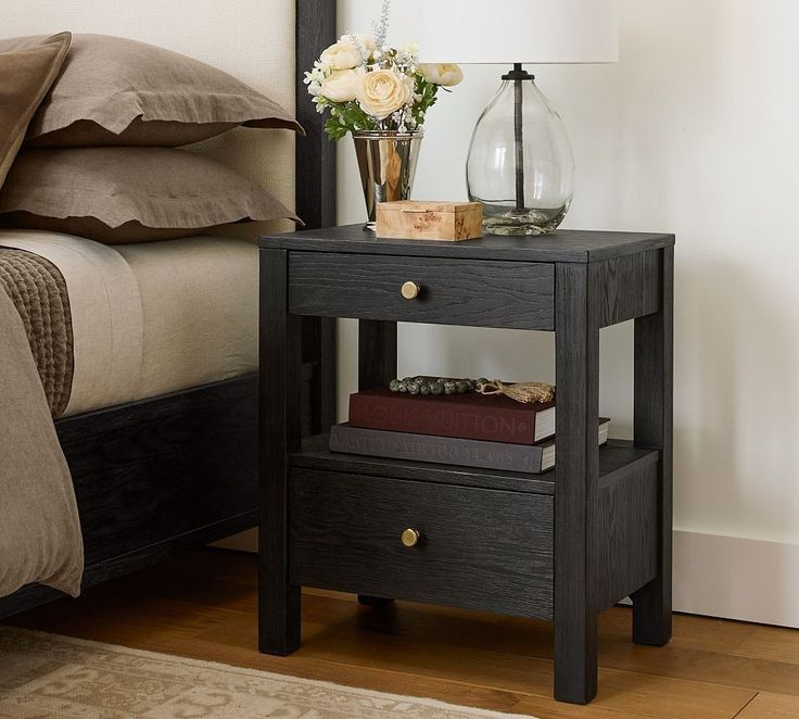 a night stand with two books on it next to a bed