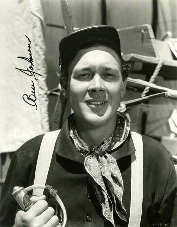 black and white photograph of a man in overalls holding a pipe with writing on it