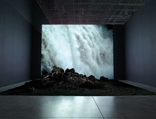 an image of a large waterfall in the middle of a room with rocks on the floor