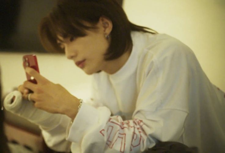 a woman sitting on a bed looking at her cell phone while wearing a white shirt