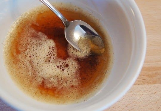 a white bowl filled with brown liquid and a silver spoon in it on top of a wooden table