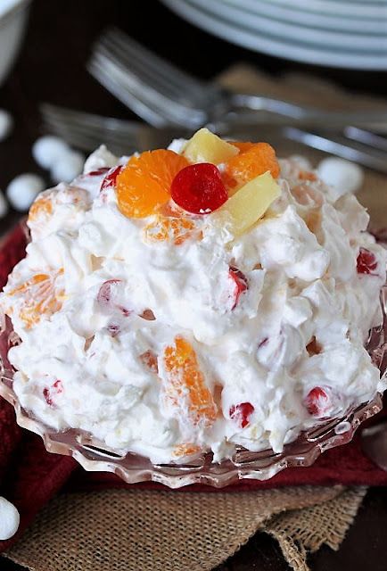 a bowl filled with fruit salad sitting on top of a red cloth next to silverware