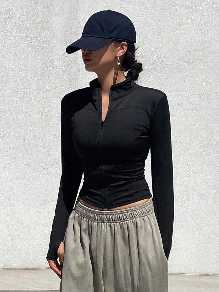 a woman wearing a black top and skirt with a baseball cap on her head standing in front of a white wall