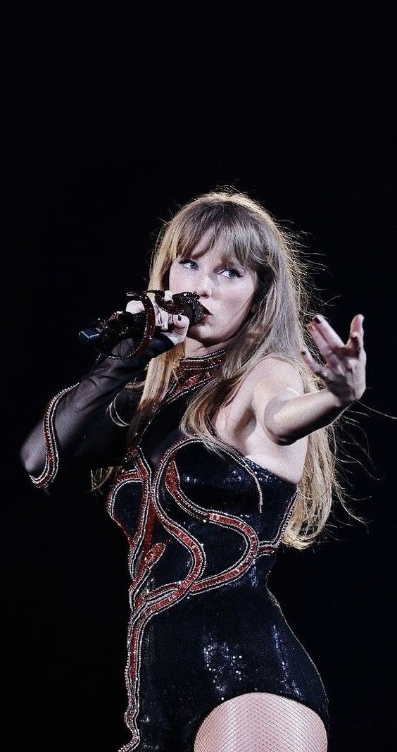 a woman in a short black dress holding a microphone and singing into the air with her right hand