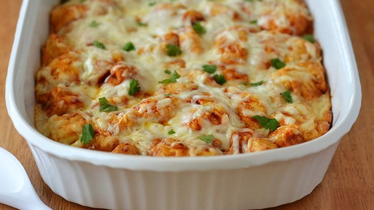 a casserole dish with meat and cheese in it on a wooden table next to a spoon