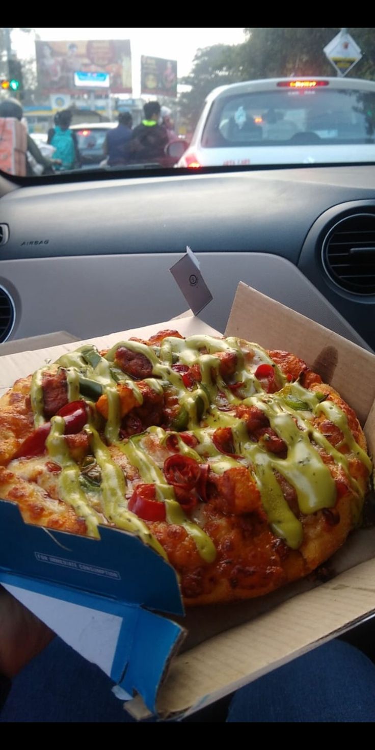 a pizza sitting inside of a box on top of a car dash board in front of a vehicle