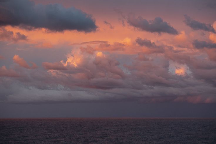 the sky is filled with pink clouds as the sun sets in the distance over the ocean