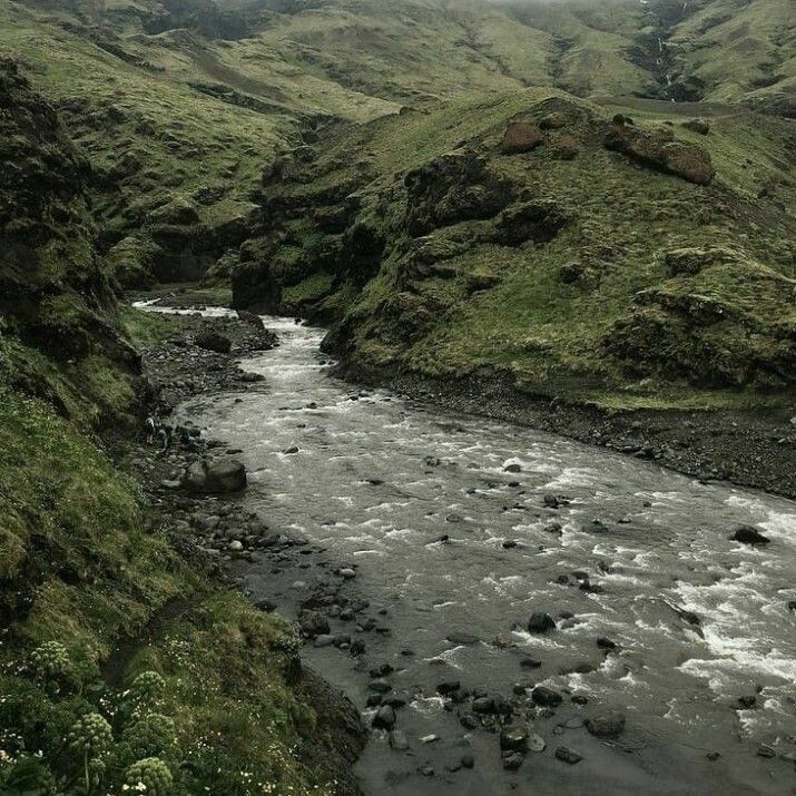 a river flowing through a lush green valley filled with grass covered hills in the distance