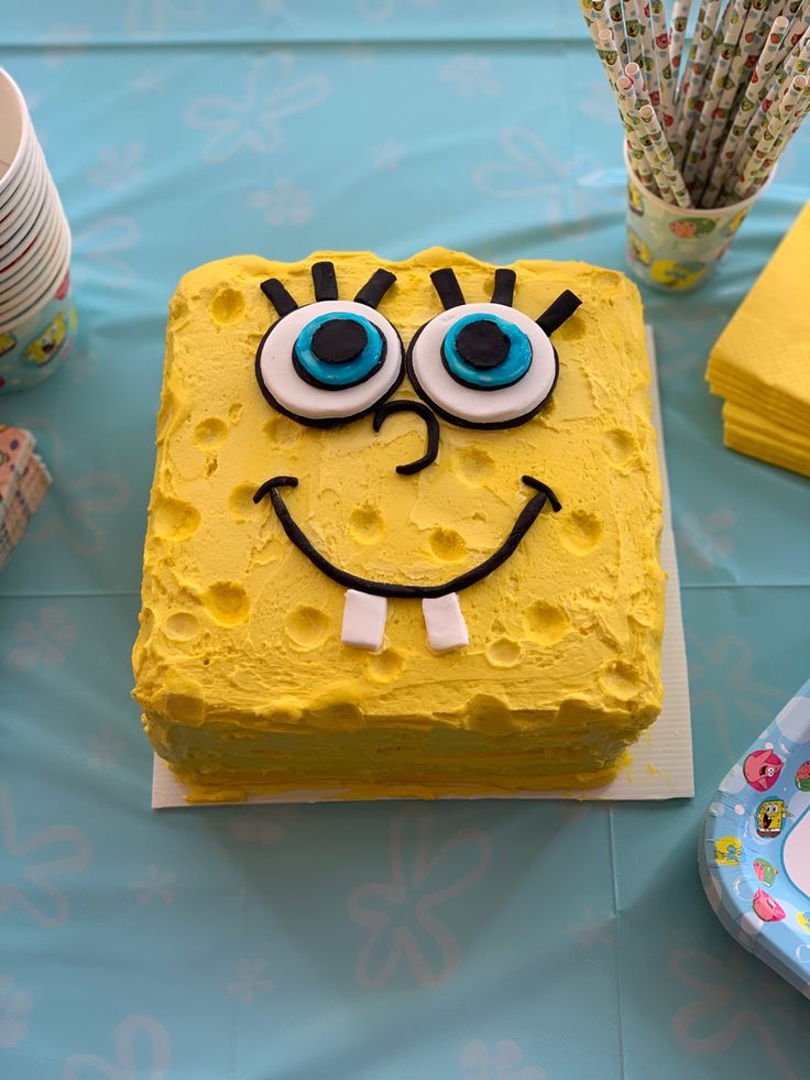 a spongebob cake on a blue tablecloth with paper straws in the background