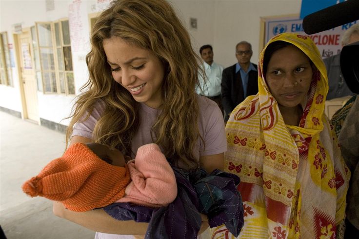 a woman holding a baby in her arms while other people look at the pictures on the wall behind her