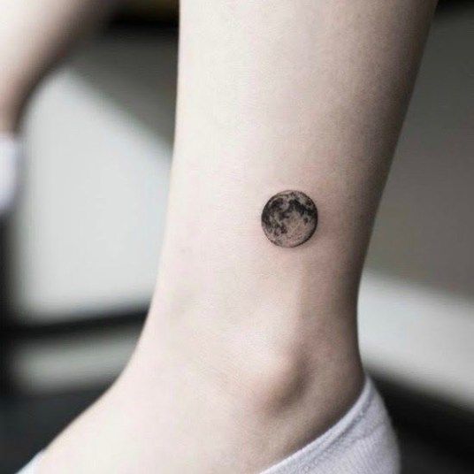 a small tattoo on the ankle of a woman's left foot, with an image of the moon above it