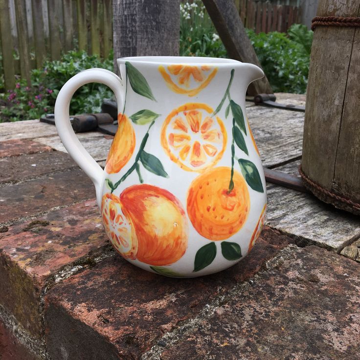 a white pitcher with oranges painted on it sitting on top of a stone slab