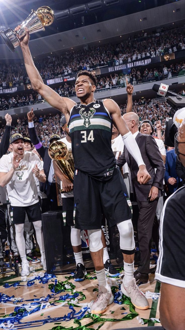 a man holding a trophy while standing on top of a basketball court with other people