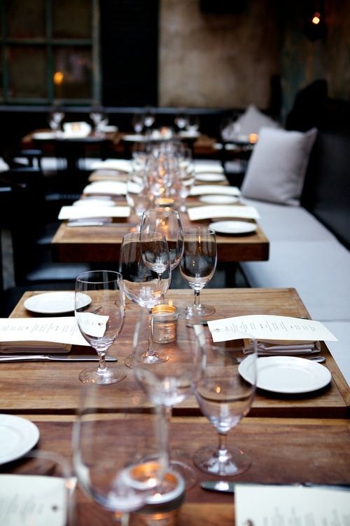 a long table is set with empty wine glasses and place settings for two people to sit at