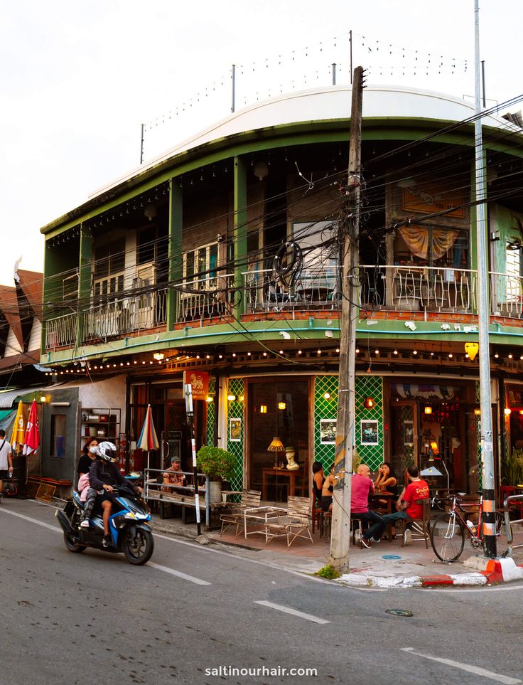 a motorcycle parked in front of a building with people sitting at tables on the outside