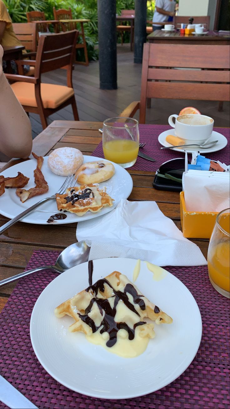 a table topped with plates of food covered in sauce and toppings next to glasses of orange juice