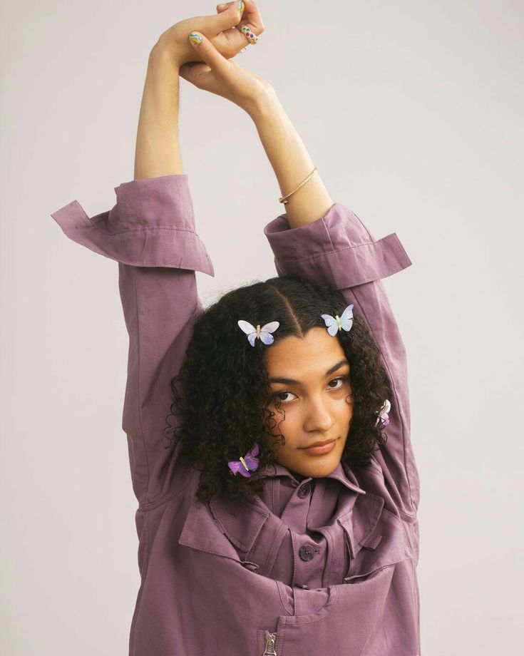 a woman with her arms up in the air and two butterflies pinned to her hair