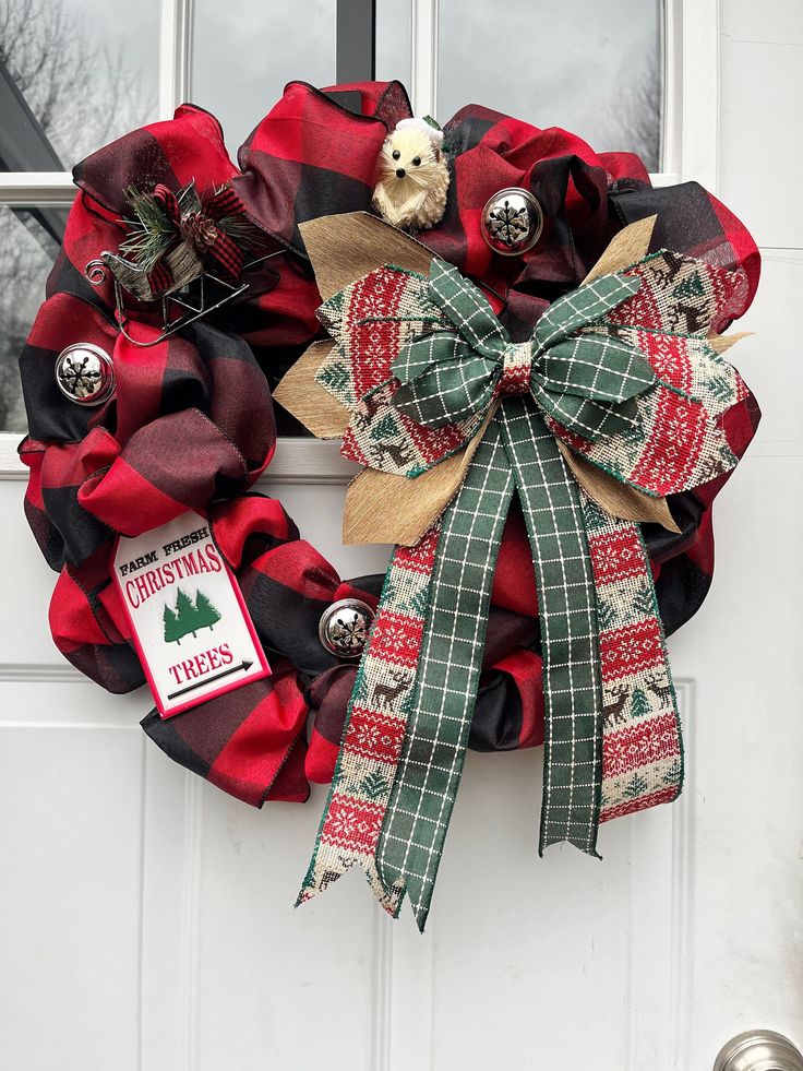 a red and black christmas wreath hanging on a white door with a dog in the center