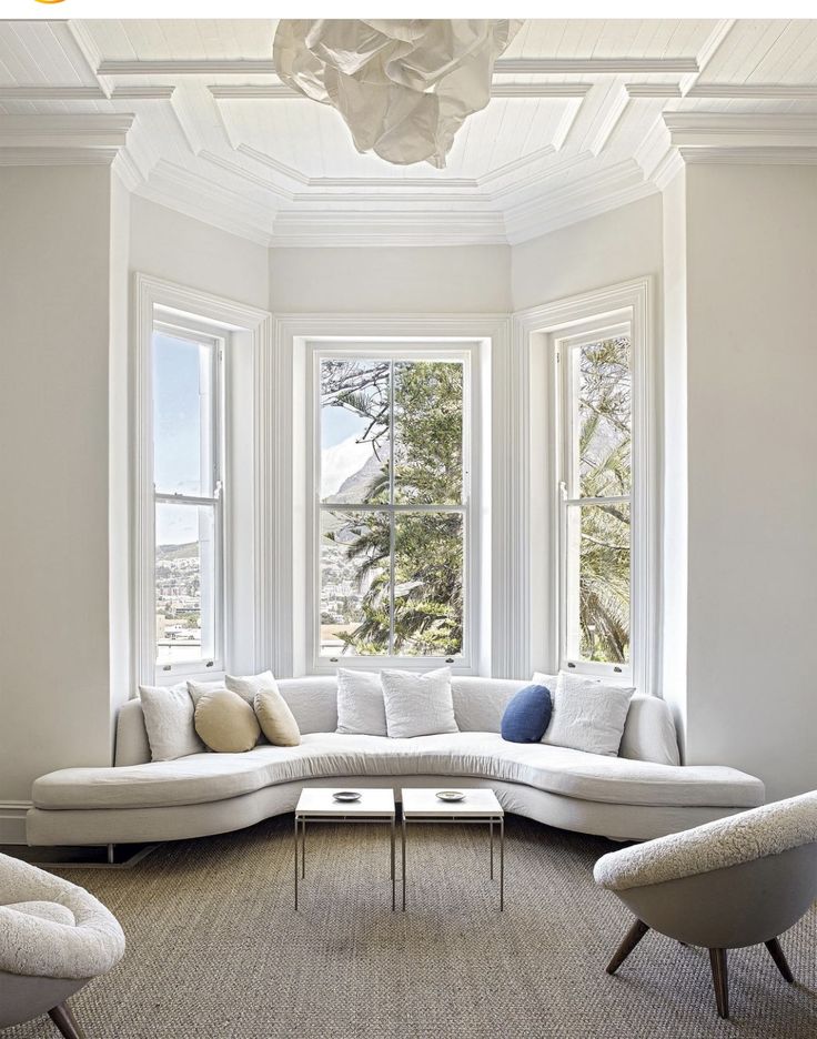 a living room filled with white furniture and large windows overlooking the city below it's trees